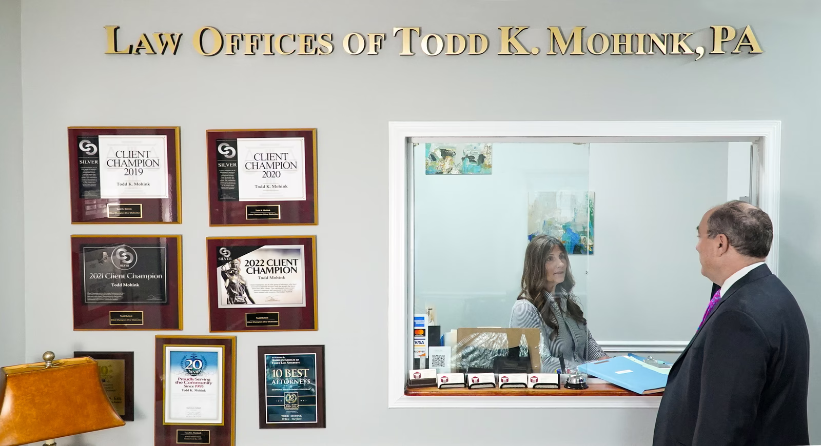 Law office reception area with client champion awards on wall and staff member greeting visitor at front desk