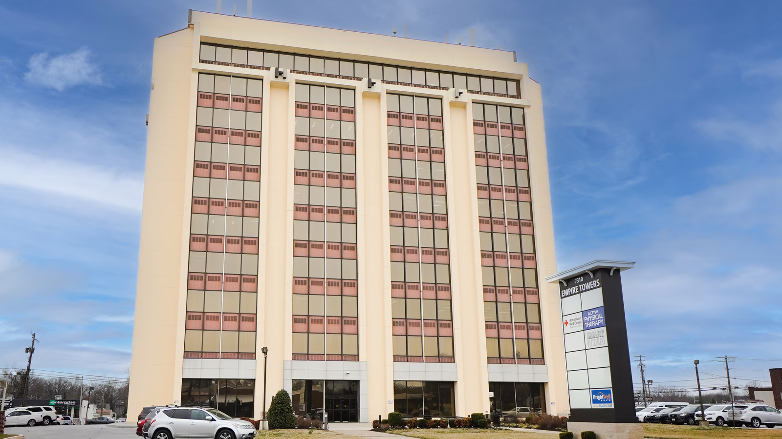 Cream-colored multi-story office building with vertical white columns and red-tinted windows